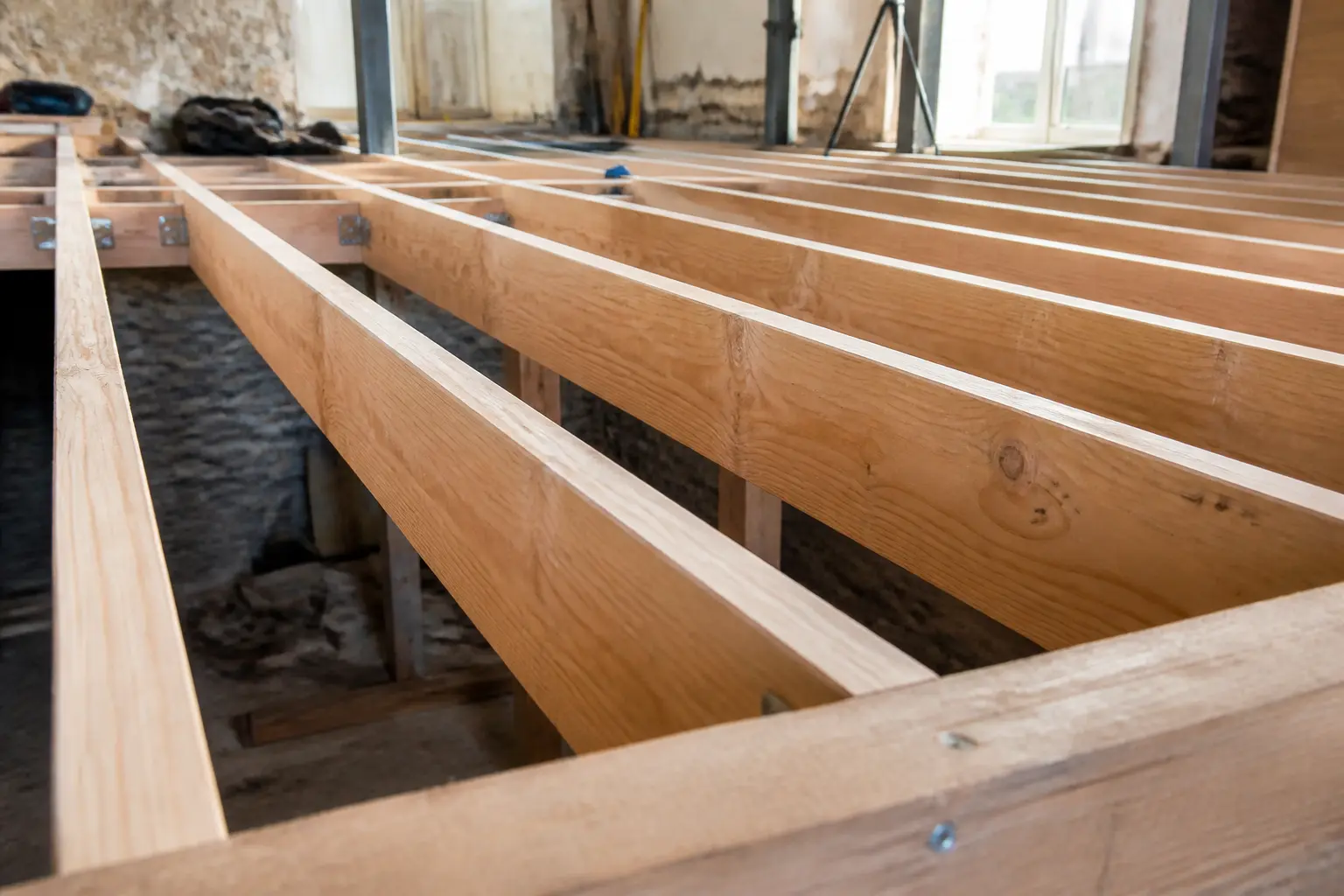 Solive en bois alignée sur un chantier, structure de plancher en rénovation avec outils et lumière naturelle
