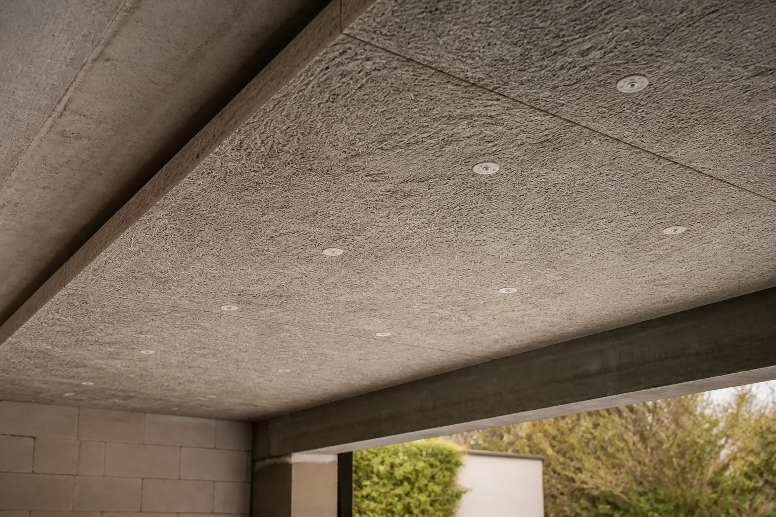 Fibralith posé sous une dalle de garage en béton, isolation fibreuse grise avec fixations visibles et lumière naturelle.