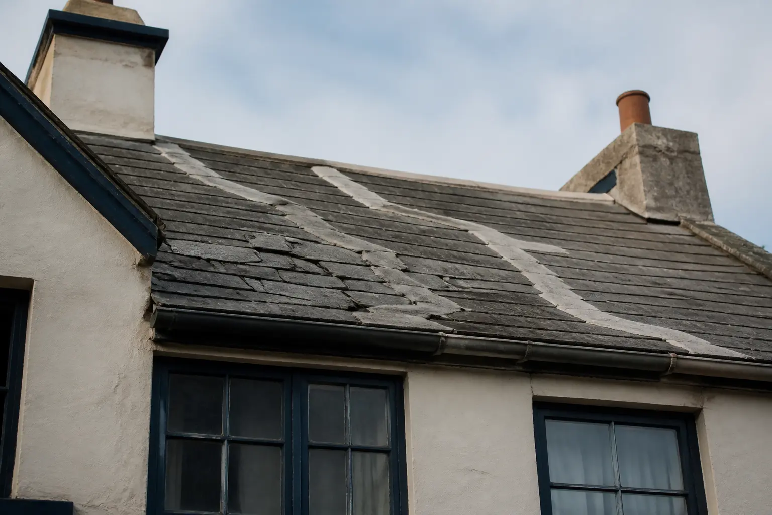 Façade d’immeuble ancien avec toiture fissurée et réparée, illustrant les dépenses de grosses réparations effectuées par les nus-propriétaires