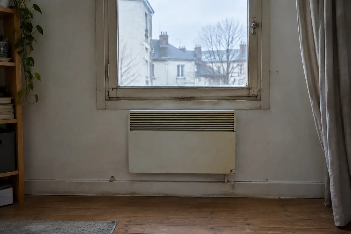 Vieux convecteur électrique sous une fenêtre à simple vitrage dans un appartement loué